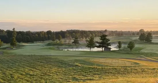 A view of a fairway as mist rises from the pond on a golf course