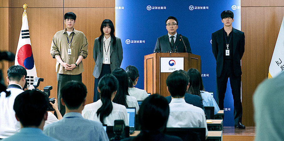 A group of four people face a group of reporters at a press conference.
