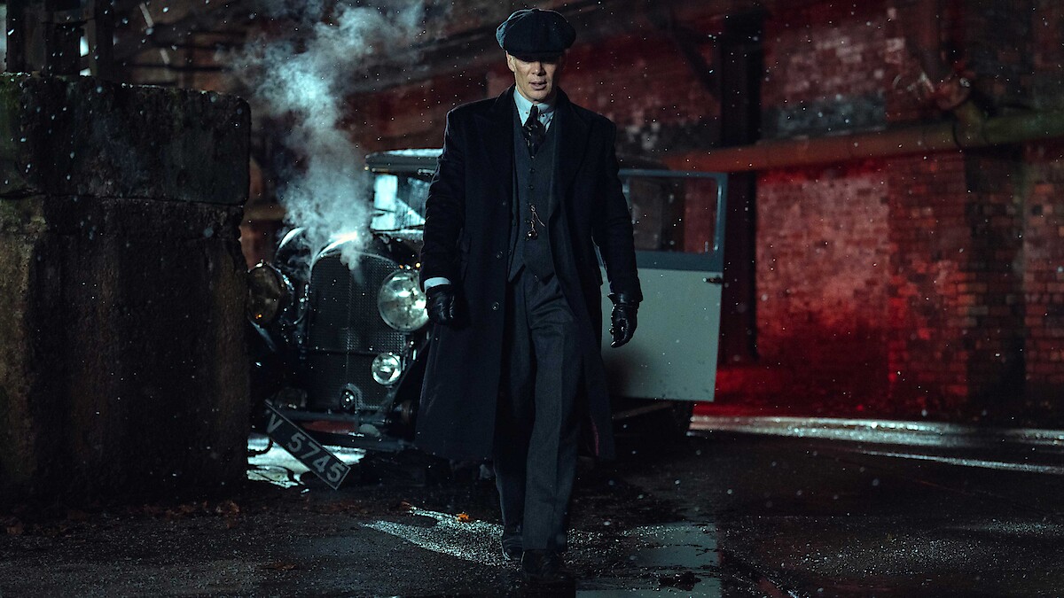 A man in 1920s attire and flat cap walks away from a vintage car with steam rising, set in a dark, industrial urban alleyway with wet pavement and red brick walls at night.