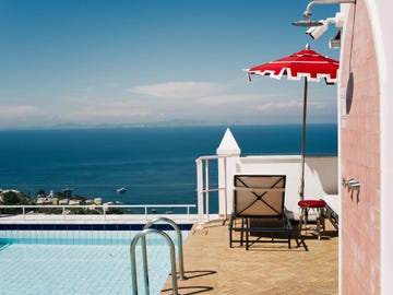 seaside pool deck with lounge chairs, red umbrella, and distant ocean view.