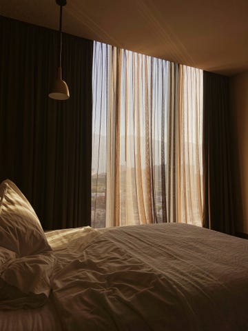 sunlight streaming through sheer curtains onto an unmade bed