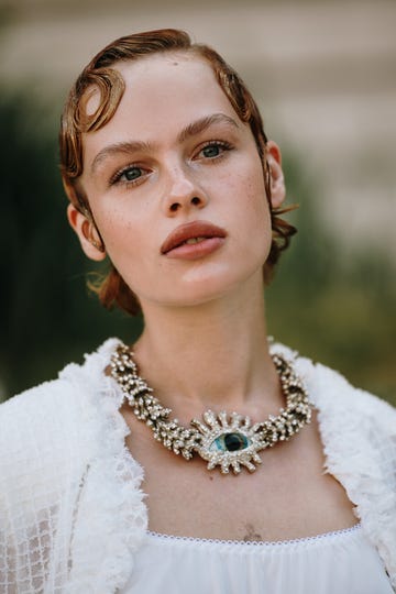 woman wearing a white outfit and a large eye shaped necklace