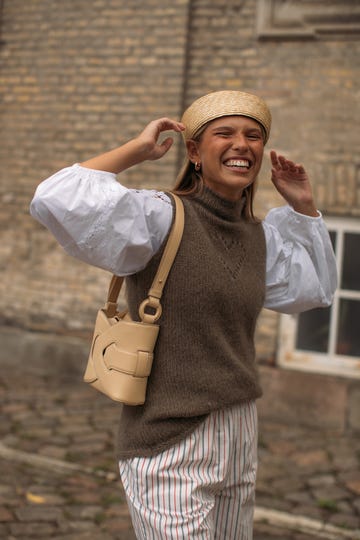 Person wearing a brown vest, white blouse, striped pants, and straw hat, smiling broadly outdoors.