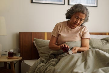 a sick old woman is taking medicine on the bed in bedroom.