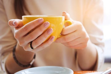 Yellow mug in the hands of a young woman. Girl holding a Cup of coffee in a cafe. Coffee break, Breakfast. The concept of power. Close up.