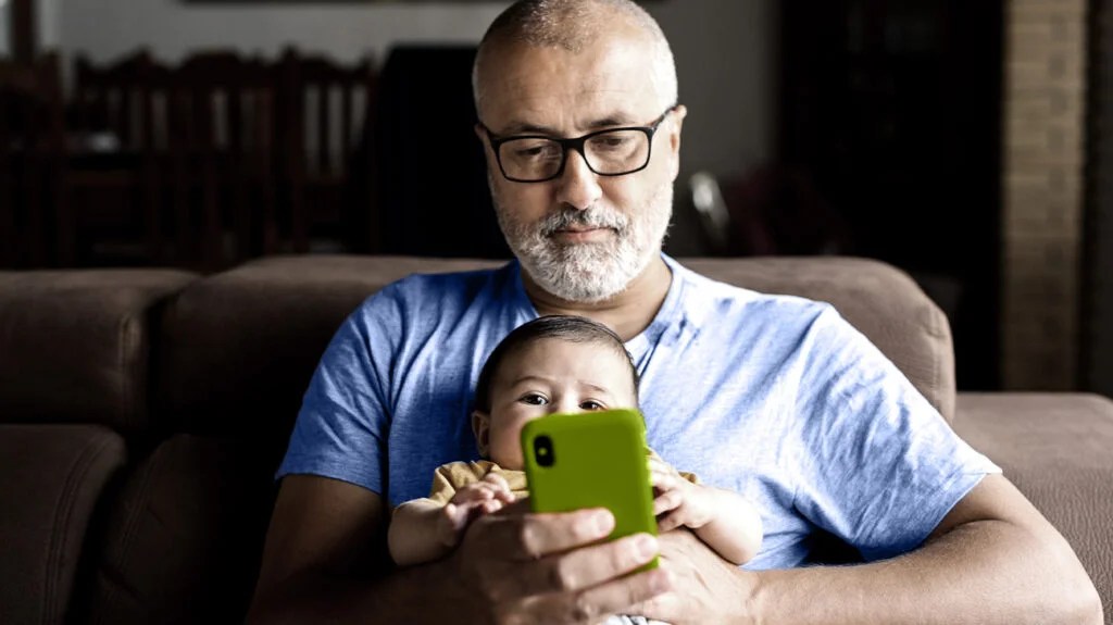 a man sat with a child and looking at his phone to see if leukemia is hereditary