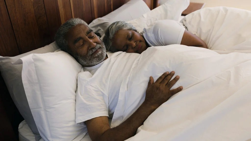An older couple hug while lying in bed. 