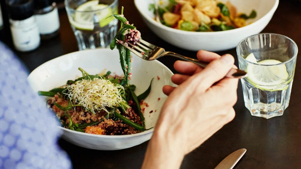 A person eat a bowl of grains and green beans