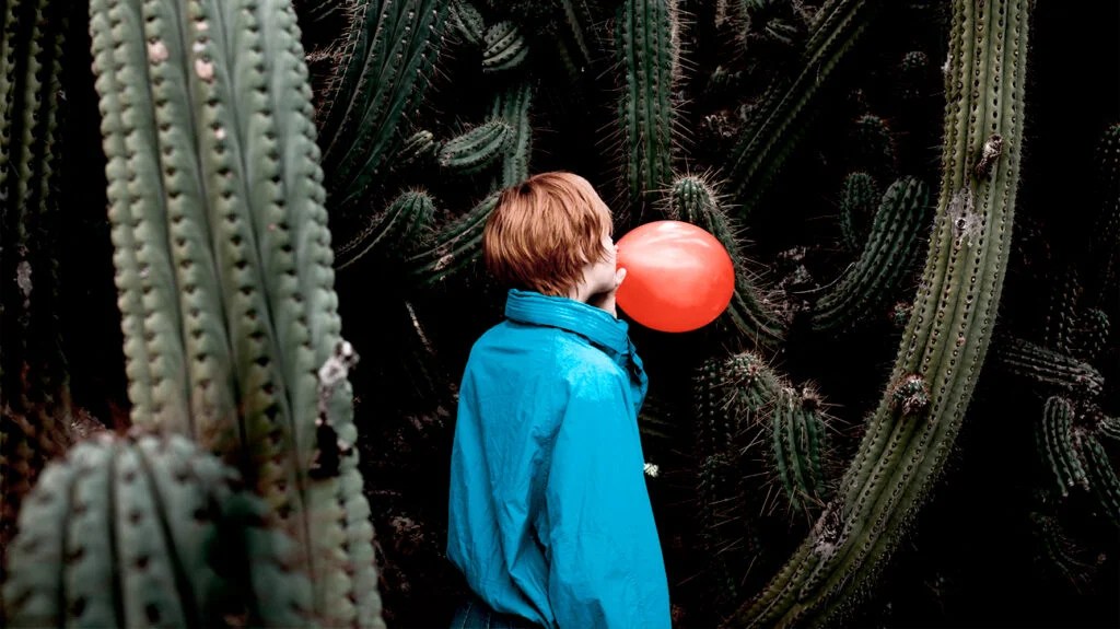 a teen with anxiety blowing up a balloon near some cacti