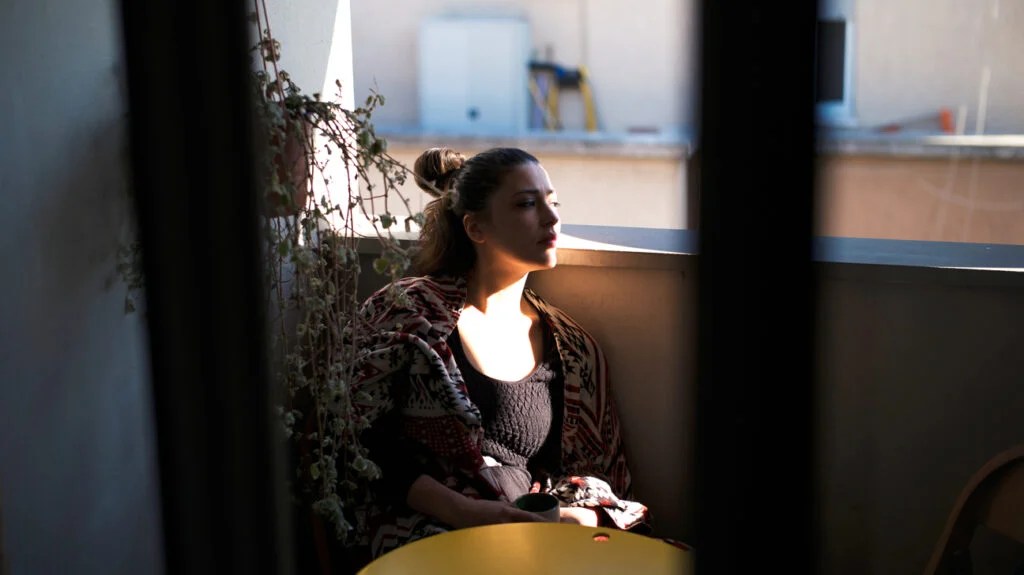 Female sat in a shaded cafe staring pensively out of a window