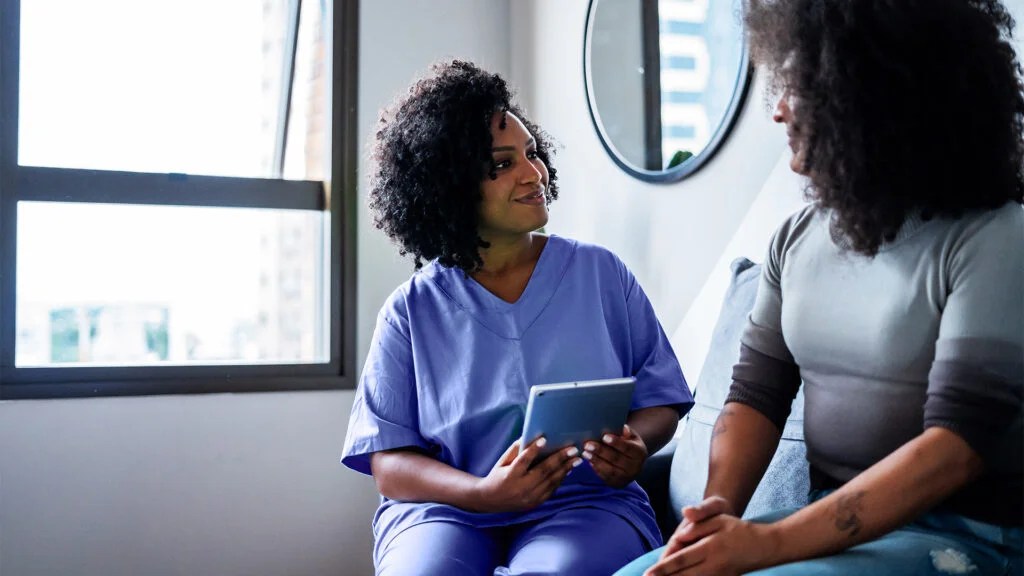 A doctor conversing with a patient, sat on a hospital bed