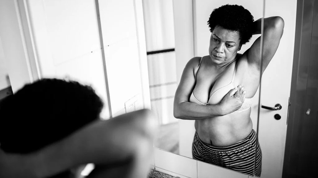 A person looking in the mirror, cupping their left breast
