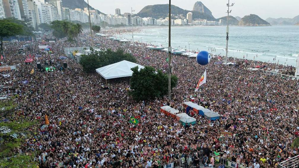 This aerial view shows demonstrators attending a protest in Rio de Janeiro against a proposed constitutional amendment and an amnesty bill on 21 September, 2025. The picture shows part of Copacabana beach filled with people. They are looking towards a stage were musicians are performing as part of the protest, but the stage can't be seen on the photo.   