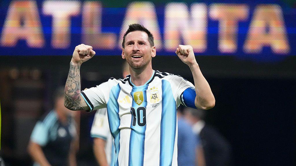Lionel Messi with both his arms up celebrating. He is wearing a blue and white Argentina shirt with the number 10 in the middle and he is smiling.