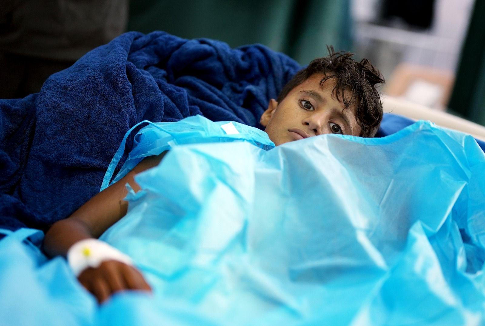 A boy called Ali, who has shrapnel injuries, lies in a hospital bed under a blue cover