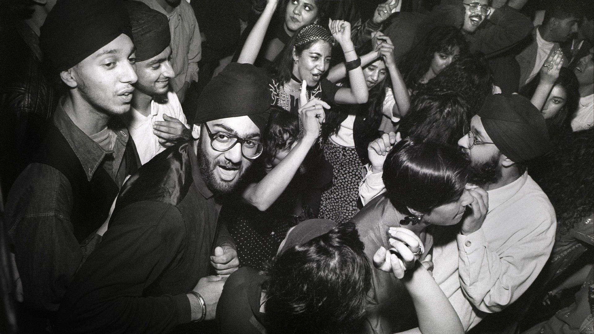 A black and white photo of a group of young people dancing joyfully. 
