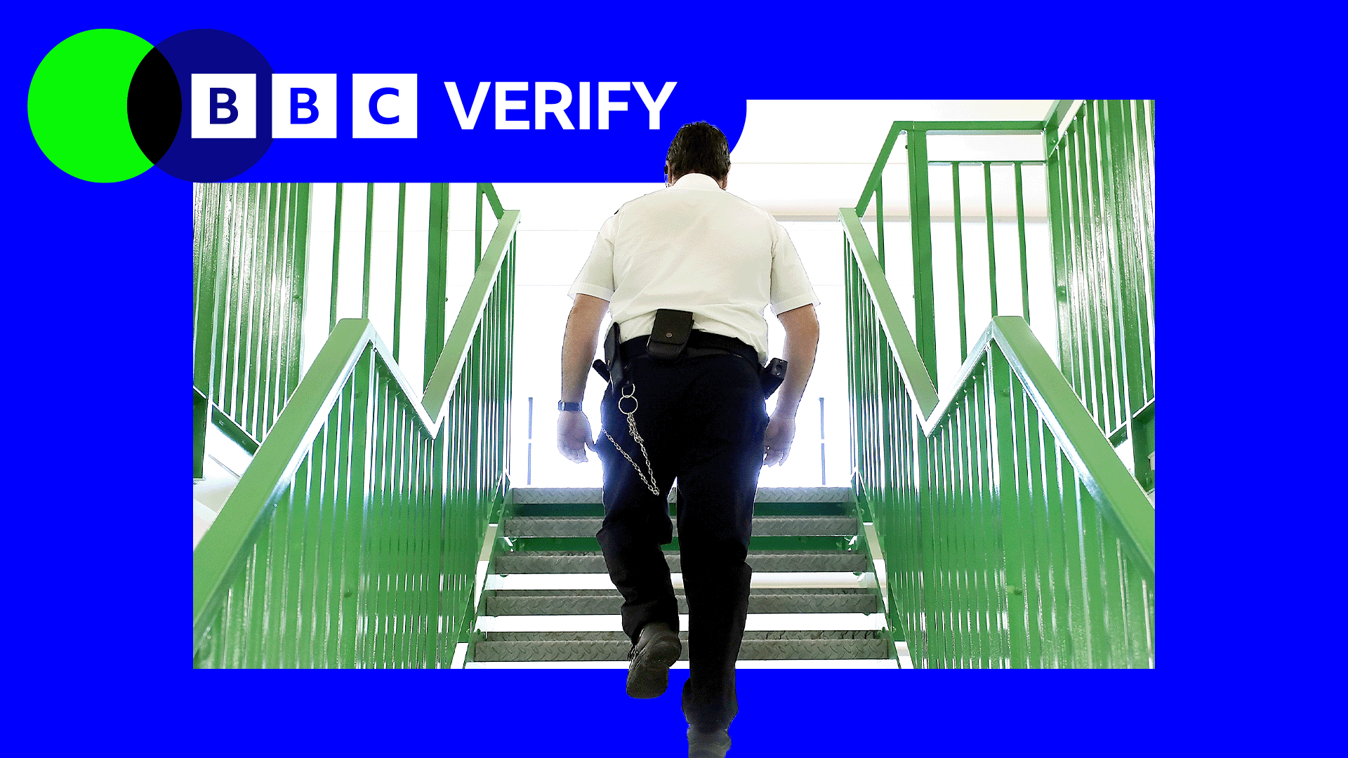 A prison officer wearing a white shirt and black trousers walks up a flight of stairs with his back to the camera.