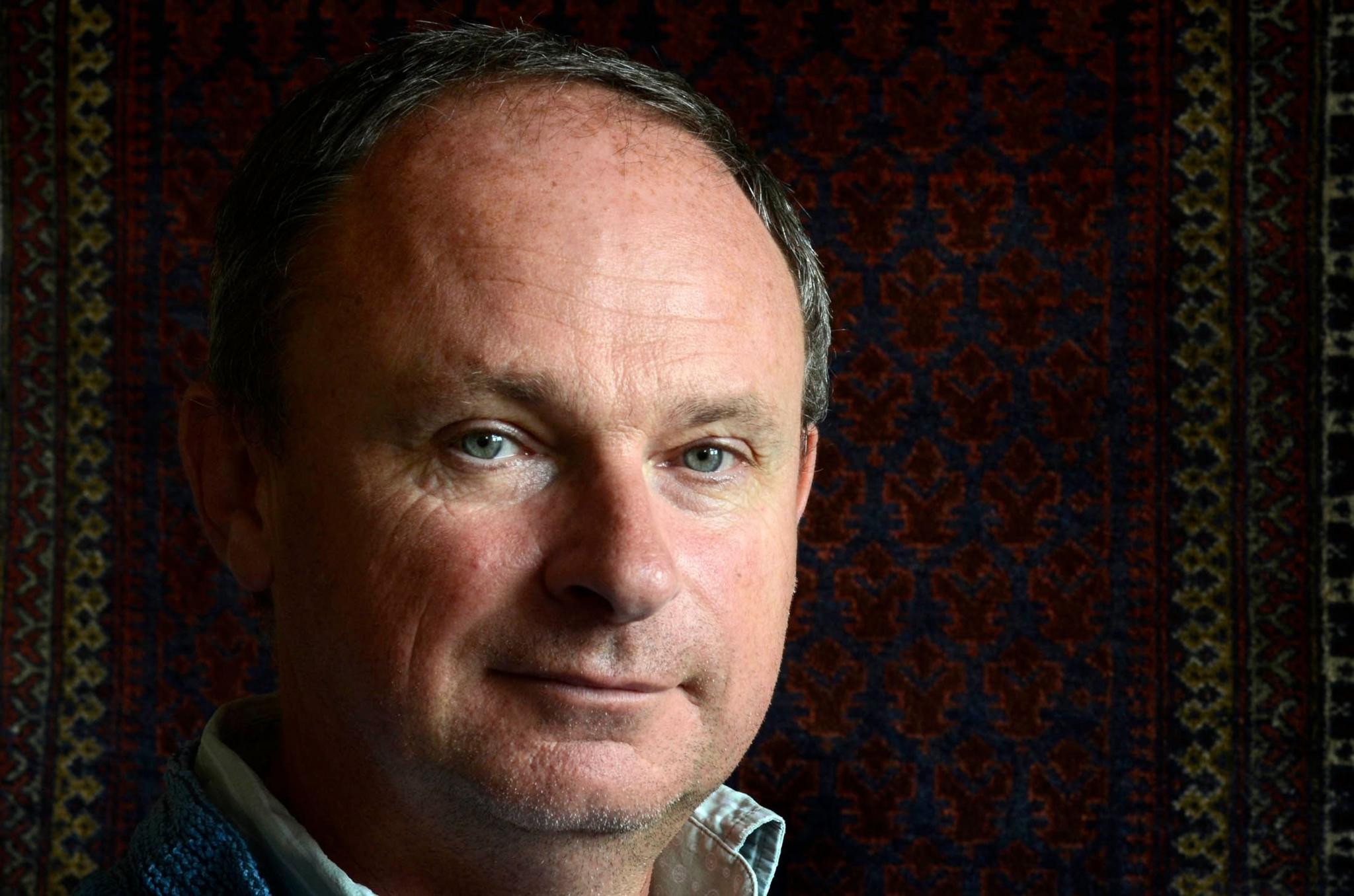A head and shoulders colour image of a middle-aged man with thinning, peppery grey, short cropped hair.