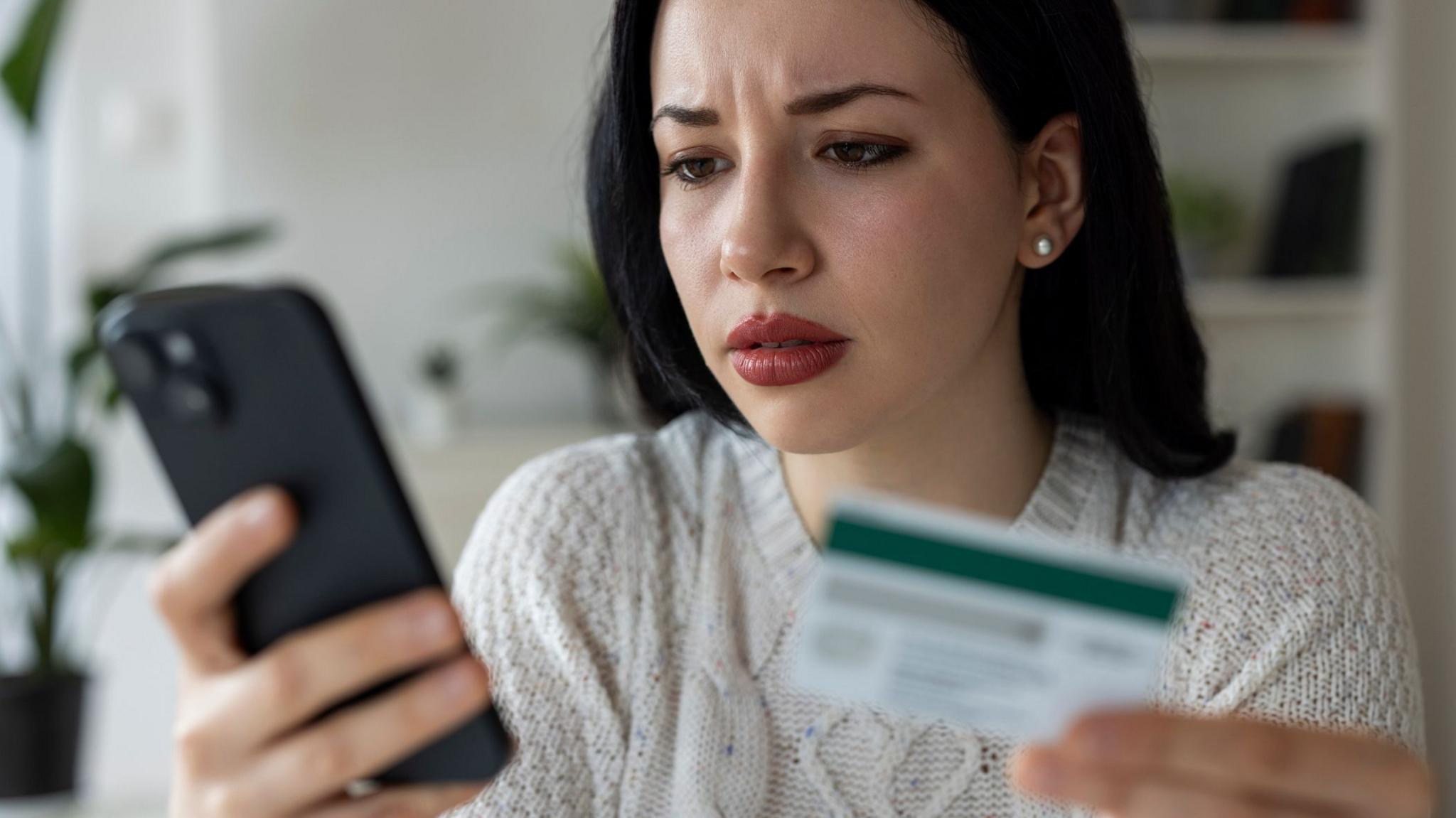 Woman with dark hair holds a credit card in one hand and a smartphone in the other.