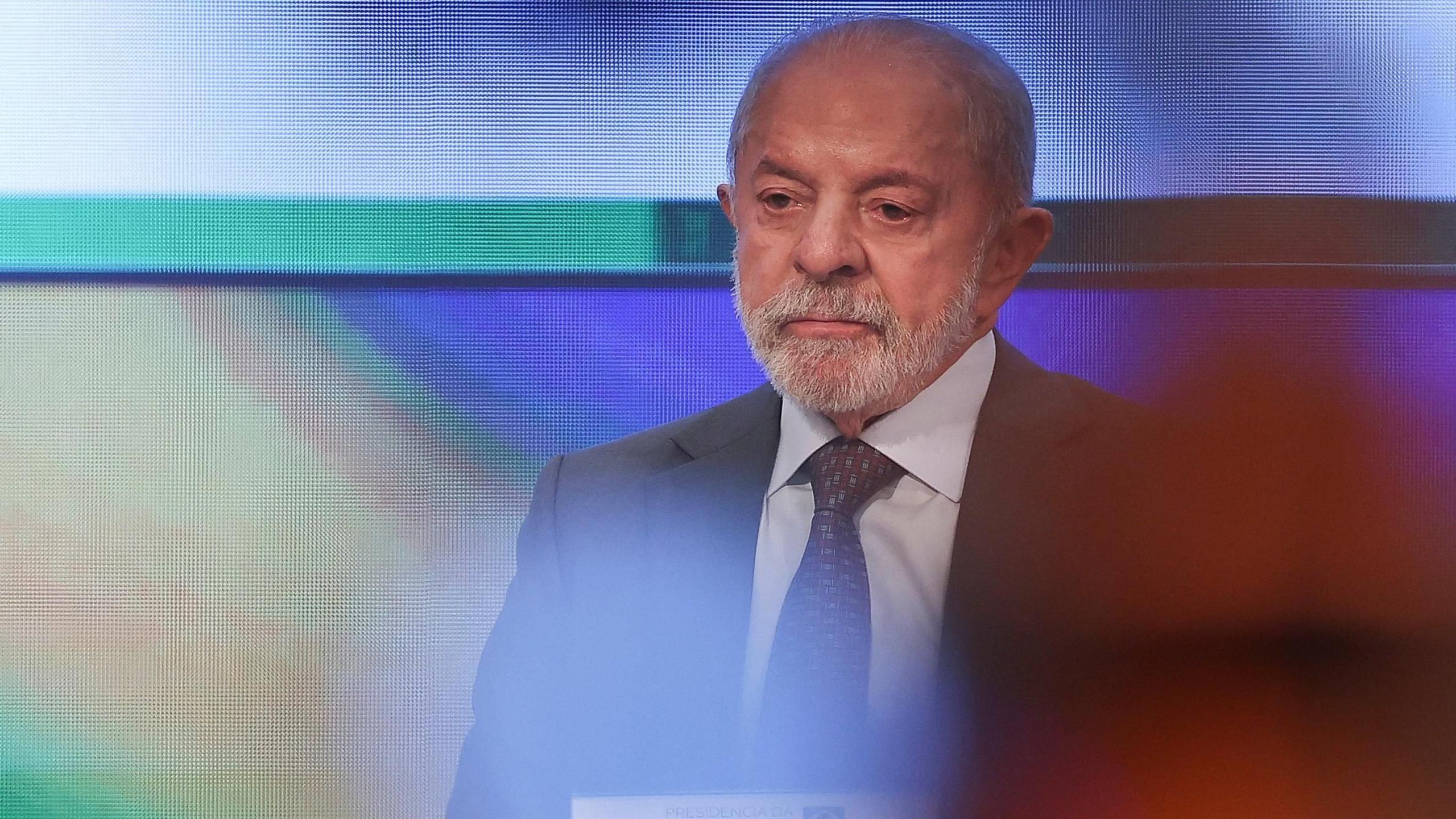 Brazil's President and candidate Luiz Inácio Lula da Silva sitting in front of a computerised screen while wearing a grey suit and purple tie. 