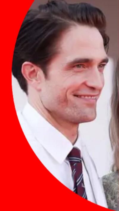 Robert Pattinson has short brown hair and is wearing a white shirt with a purple, blue and white tie.