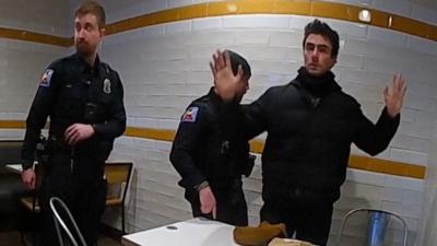 A man with his hands in the air about to be searched by a police officer in a McDonald's.
