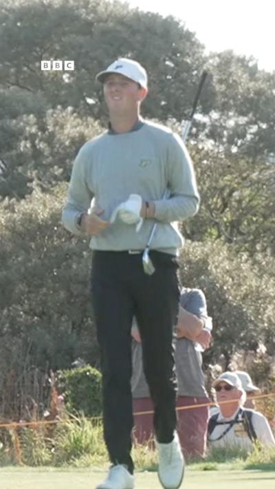 Golfer Sam Easterbrook, wearing a white cap and grey jumper, walks with his club tucked under his arm