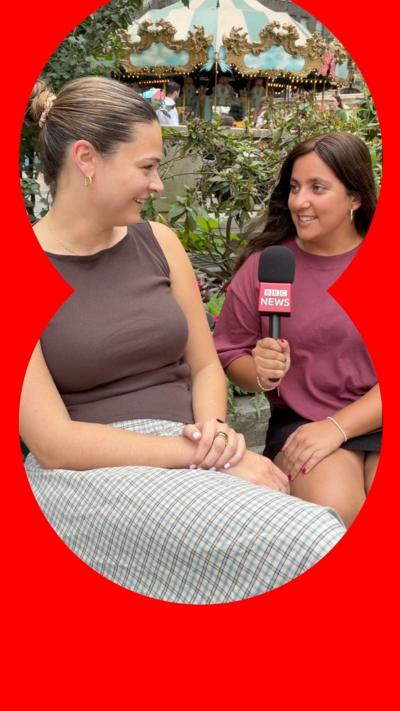 Two women sit together, one holds a microphone