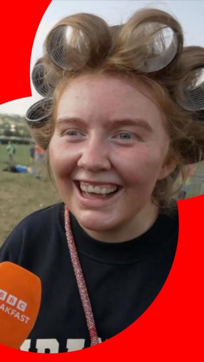 A smiling woman with rollers in her hair, standing in a field