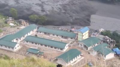 A large wave of greyish water is seen forming next to several white buildings with green roofs