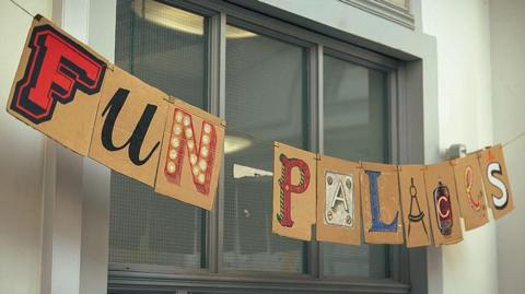 A cardboard sign strung across a window that reads: Fun Palaces. The individual letters are displayed in different fonts and colours.