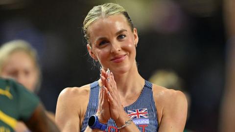 Head and shoulders of Keely Hodgkinson, wearing a blue GB vest with thin white stripes, standing with her hands together in front of her chest