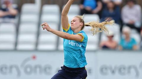 Alexa Stonehouse in sky blue shirt and navy blue trousers bowls for Warwickshire