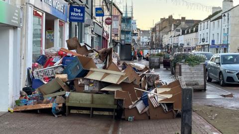 A pile of furniture and items placed on a pavement in a high street in front of shops, after it was hit by heavy rain.