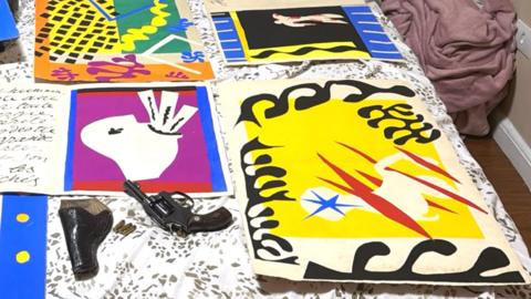 he Matisse illustrations - bold cut out collages in primary colours and black - are pictured laid out on a bed, alongside a handgun