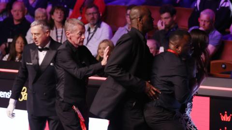 A female spectator (right) is escorted out of the arena at the Crucible Theatre in Sheffield after jumping the barrier between the seats and the playing area