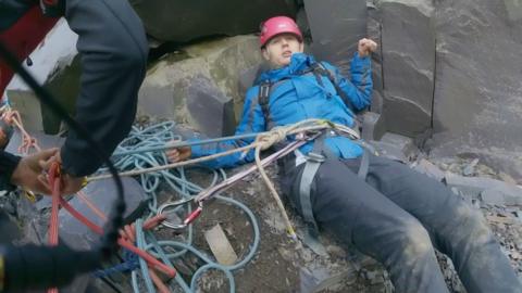 Man on rocks in climbing gear being rescued 