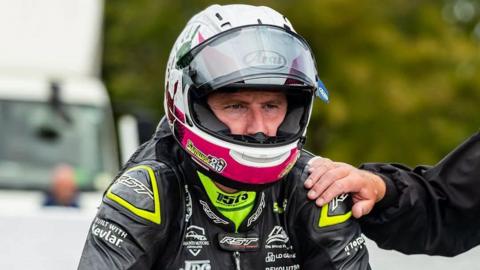 Same Naughton on the start line in his helmet and leathers with the starter's hand on his shoulder.