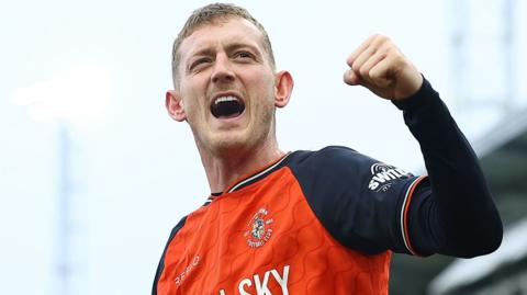 George Saville celebrating having scored a goal for Luton. He is wearing the orange and navy home shirt.