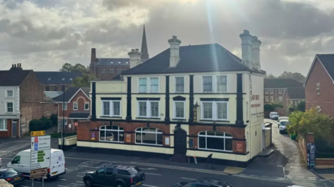 This picture shows the Sky Blue Chinese Restaurant in York. It is a large, detached building which has eight large windows. The lower third of the building is red-brick, the rest of it is painted pale yellow. The restauarant is at the side of a busy road, traffic is driving past.