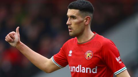 Conor Wilkinson is seen giving a teammate the thumbs up, wearing Walsall FC red home kit with club badge