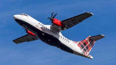 A propeller engine Loganair aircraft in flight. The plane has a white fuselage and tartan decal on its tail. The aircraft is pictured against a cloudless blue sky.