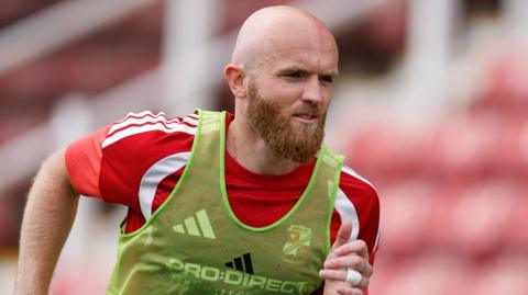Jonny Williams wearing a red Swindon Town training top with a light green bib over the top