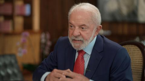 Brazil's President Luiz Inácio Lula da Silva, in a red spotted tie, dark blue suit and light blue shirt, sits in the presidential palace for an interview with the BBC