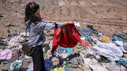 A woman holding up clothing, a red coat, that has been dumped in a desert in northern Chile