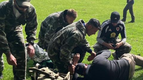 A group including Willy Caballero (left), Aaron Ramsey (second right) and Luke Williams (right) tend to a casualty during a military training exercise as part of the FAW's Uefa pro licence course