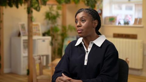 Kemi Badenoch in a blue collared shirt.