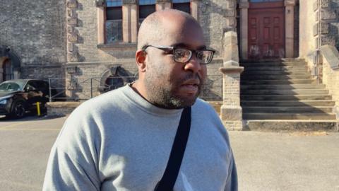 A prisoner stood outside HMP Wandsworth in a grey sweathshirt and glasses