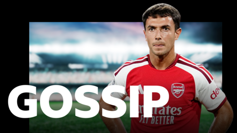 Martin Zubimendi, with his hands on his hips in a football shirt with a red body and white short sleeves, with 'gossip' written across the bottom of the graphic in white capital letters