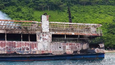 The ruins of the ferry MV June Aster are seen following a fire that broke out. Partial view of the ship with green hills beyond.
